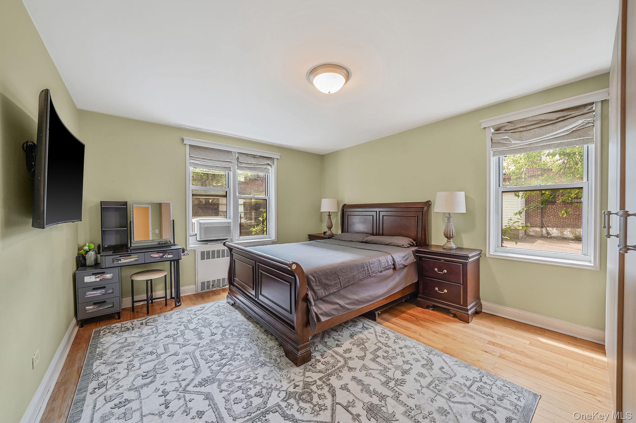 103-26 68th Avenue, Unit 2E Queens, NY 11375 - Photo 15 of 22 Bedroom with radiator heating unit, wood finished floors, multiple windows, and baseboards