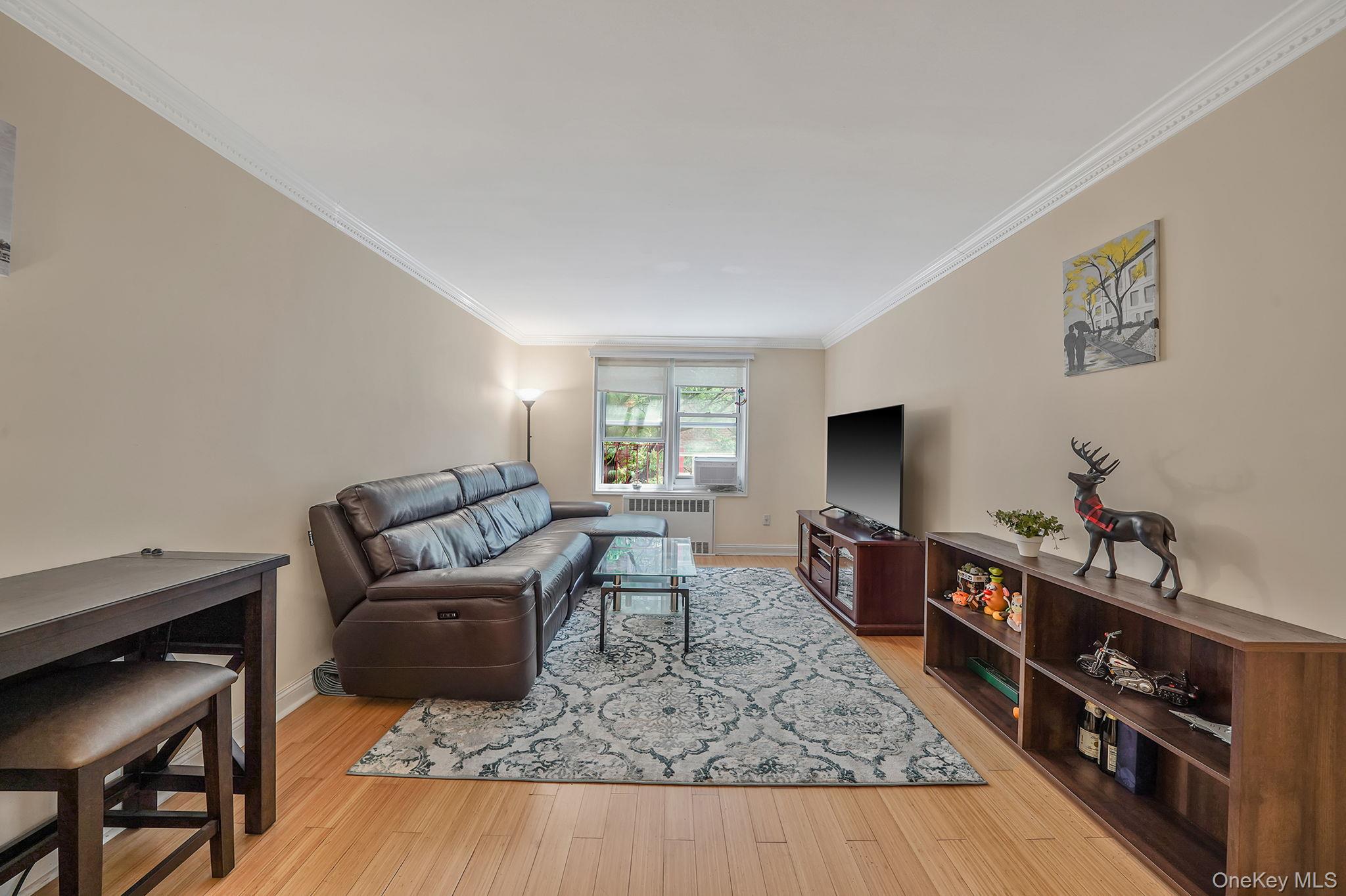 103-26 68th Avenue, Unit 2E Queens, NY 11375 - Photo 8 of 22 Living area featuring radiator heating unit, ornamental molding, baseboards, and wood finished floors
