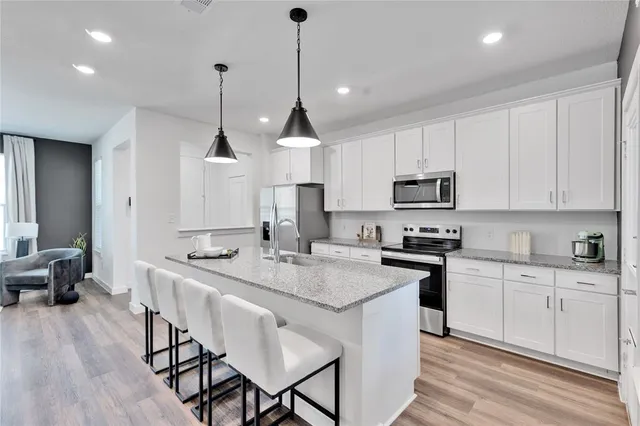 a open kitchen with stainless steel appliances granite countertop a stove a sink a oven a dining table and chairs with wooden floor