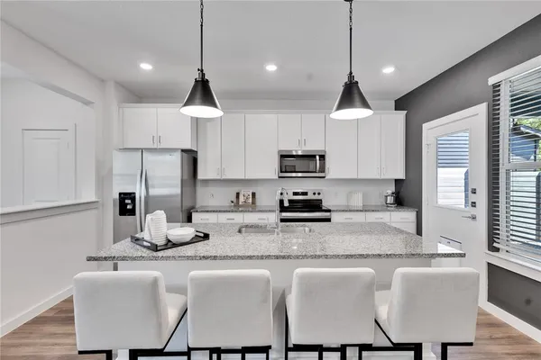 a kitchen with stainless steel appliances granite countertop a dining table chairs sink refrigerator and microwave