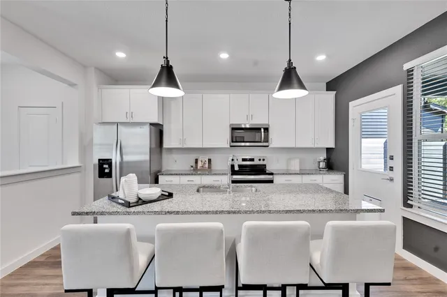 a kitchen with stainless steel appliances granite countertop a dining table chairs sink refrigerator and microwave