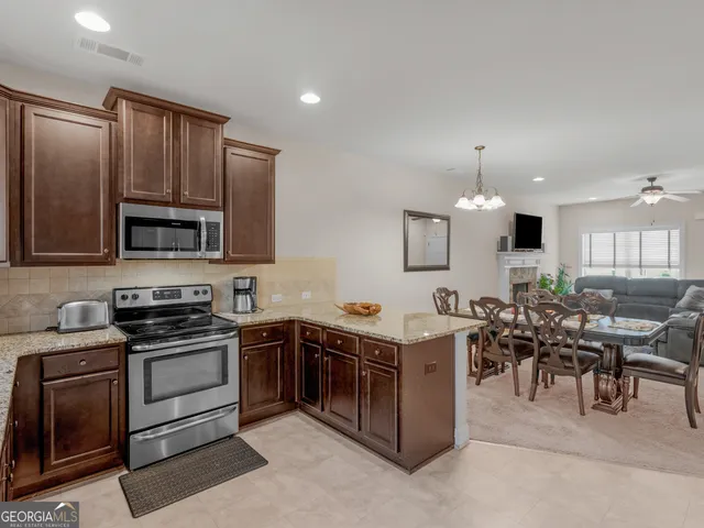 a kitchen with stainless steel appliances granite countertop a stove top oven a sink dishwasher a dining table and chairs with wooden floor