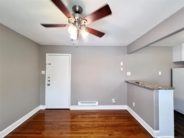 a view of an empty room with wooden floor and a ceiling fan