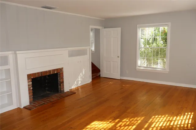 a view of an empty room with wooden floor fireplace and a window