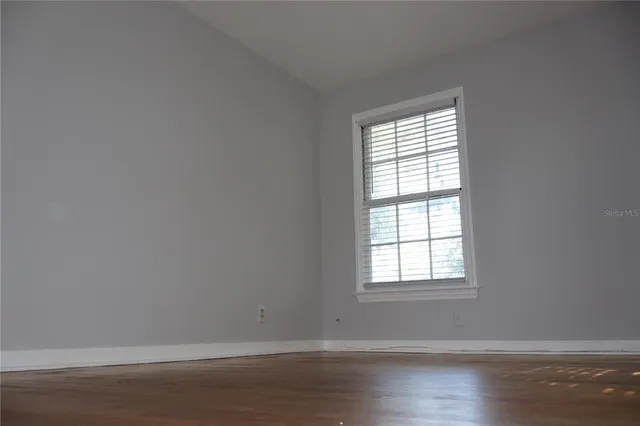 a view of an empty room with wooden floor and a window