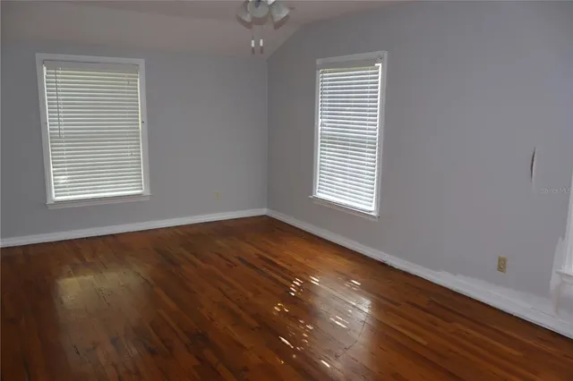 an empty room with wooden floor chandelier fan and windows