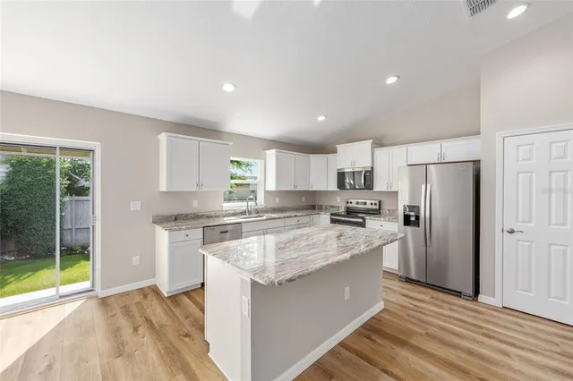 a kitchen with stainless steel appliances granite countertop a stove top oven a refrigerator a sink and dishwasher with white cabinets