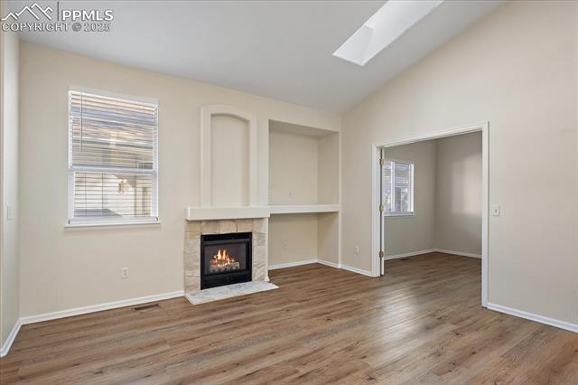1110 Samuel Point Colorado Springs, CO 80906 - Photo 8 of 28 Unfurnished living room with a fireplace, wood finished floors, vaulted ceiling, and a skylight