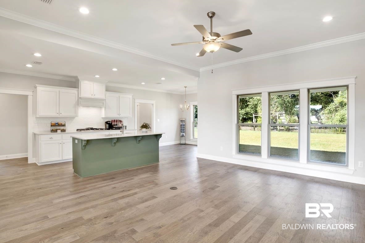 393 Garrison Boulevard Fairhope, AL 36532 - Photo 10 of 40 Kitchen with crown molding, ceiling fan with notable chandelier, white cabinetry, a breakfast bar area, and a kitchen island with sink