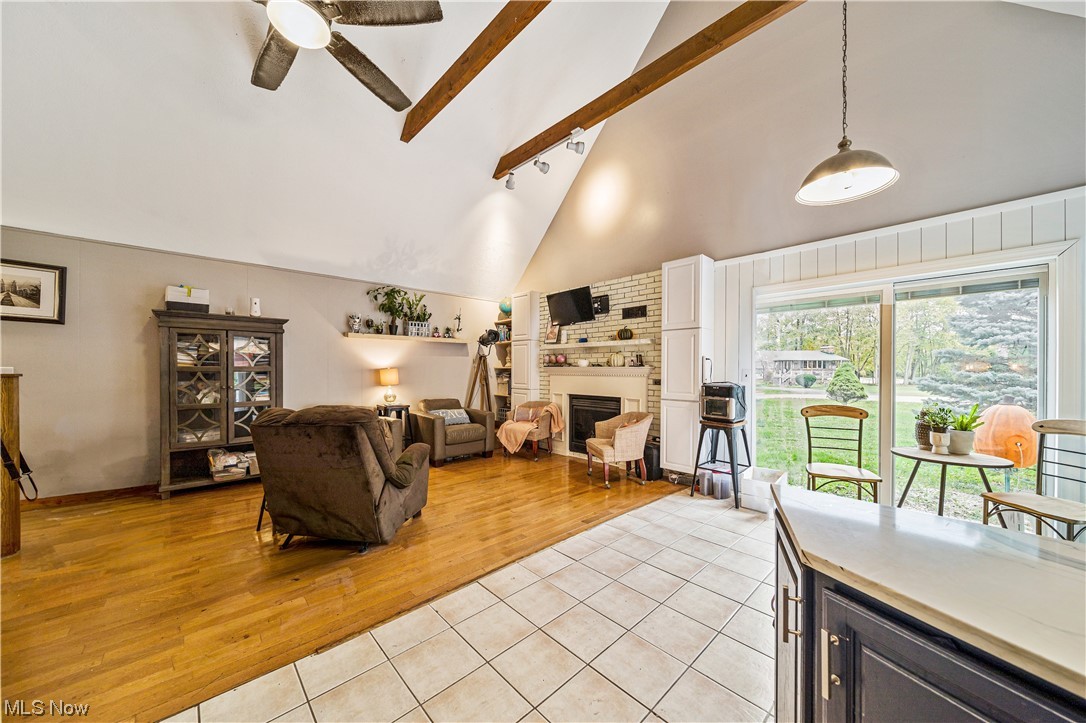 933 Long Shadow Lane Rome, OH 44085 - Photo 20 of 25 Tiled living room featuring high vaulted ceiling, ceiling fan, beam ceiling, brick wall, and a fireplace