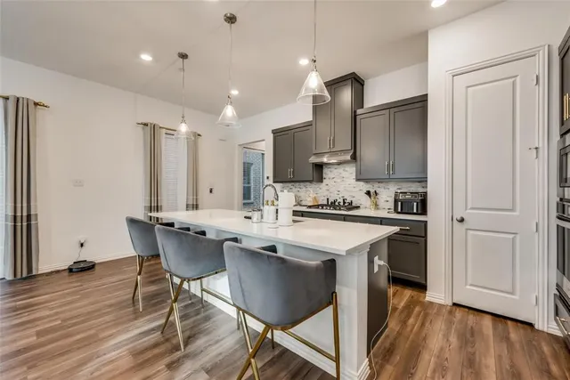 a kitchen with stainless steel appliances kitchen island granite countertop a refrigerator a stove a sink dishwasher and a dining table with wooden floor