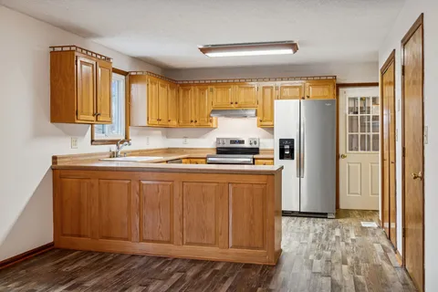 a kitchen with stainless steel appliances granite countertop a refrigerator a sink and white cabinets with wooden floor