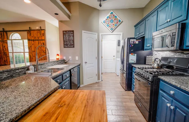 a kitchen with stainless steel appliances granite countertop a stove top oven a sink dishwasher a dining table and chairs with wooden floor