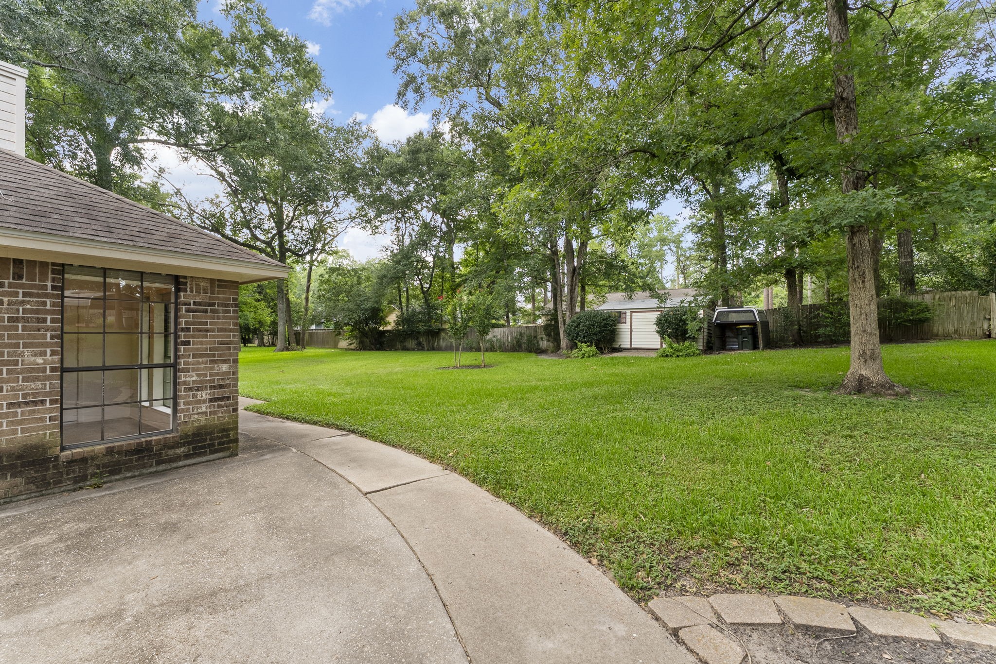202 Sunset Boulevard Conroe, TX 77303 - Photo 37 of 50 This inviting backyard patio offers a serene escape with lush greenery, mature trees, and a spacious lawn perfect for relaxation or entertaining.