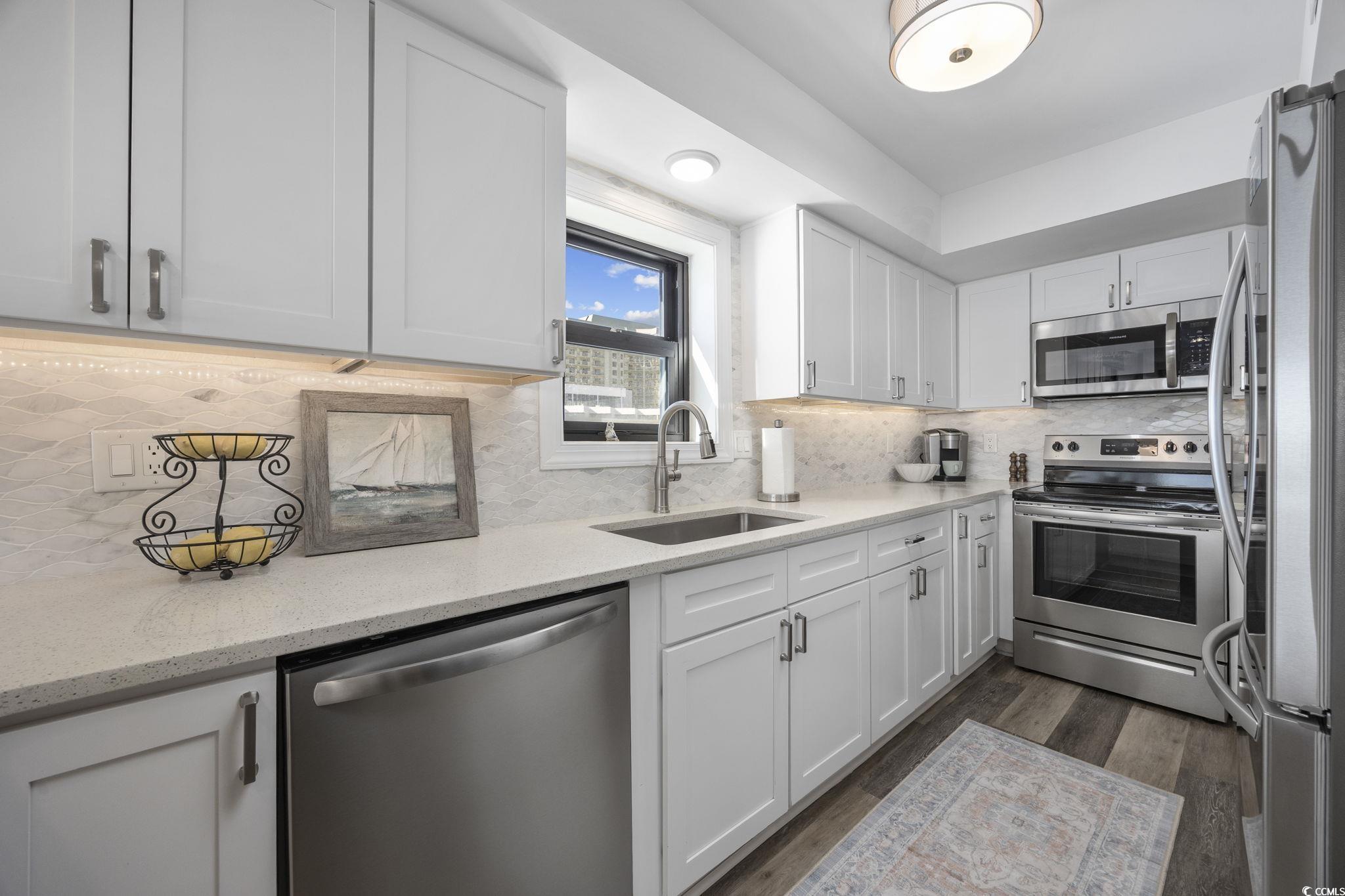 10100 Beach Club Drive, Unit 14F Myrtle Beach, SC 29572 - Photo 16 of 40 Kitchen featuring stainless steel appliances, decorative backsplash, white cabinetry, light stone countertops, and dark wood-style flooring