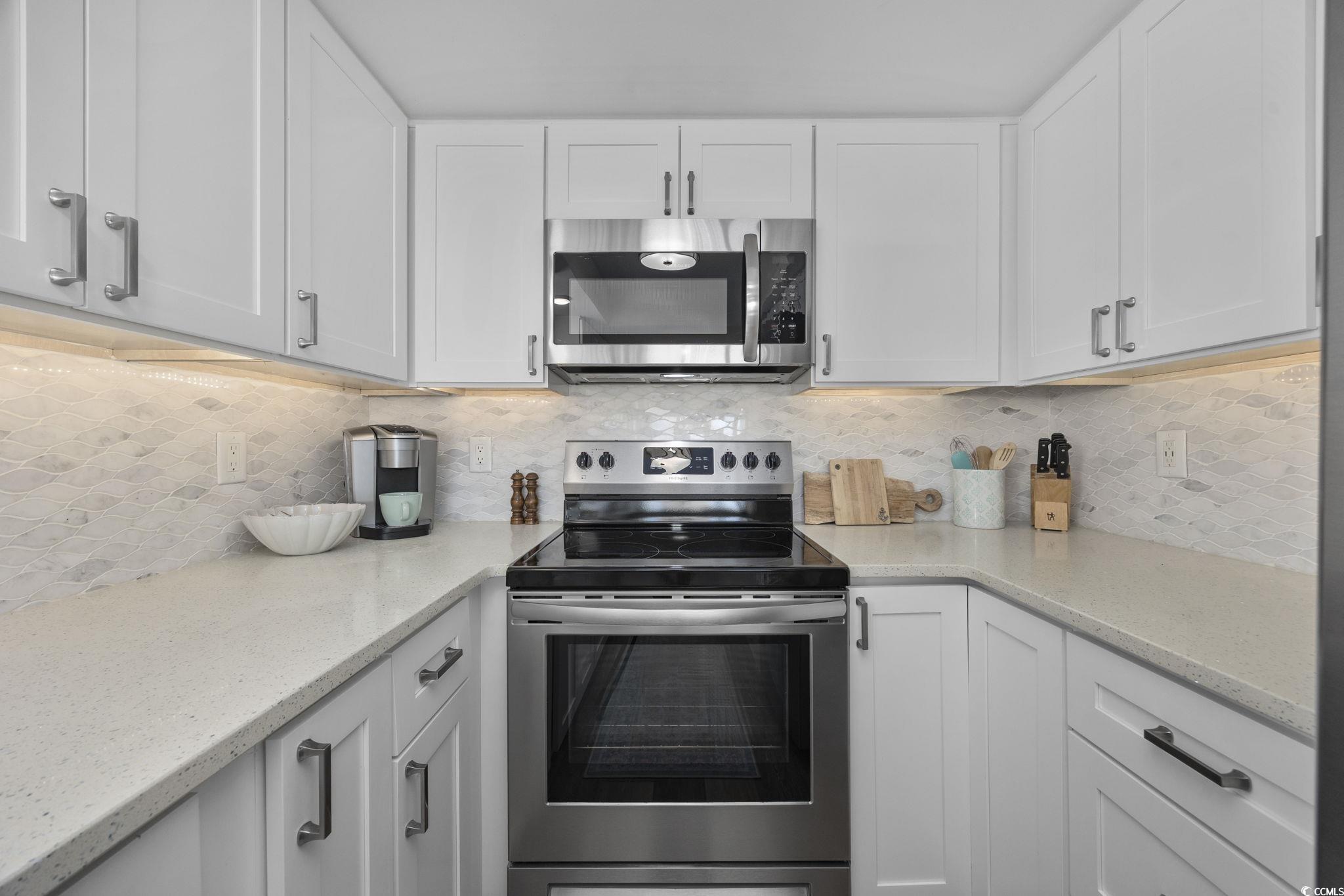 10100 Beach Club Drive, Unit 14F Myrtle Beach, SC 29572 - Photo 17 of 40 Kitchen featuring appliances with stainless steel finishes, backsplash, white cabinetry, and light stone counters
