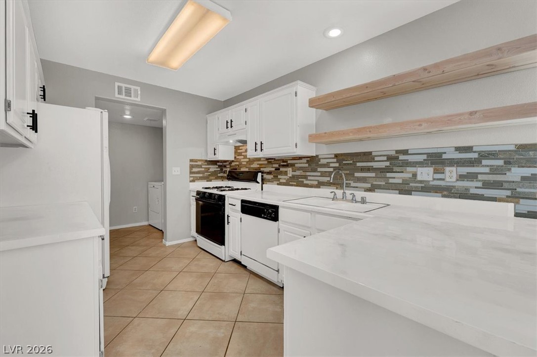 10148 Tree Bark Street Las Vegas, NV 89183 - Photo 11 of 37 Bright white cabinetry and open shelving complement a contemporary tiled backsplash in this kitchen.