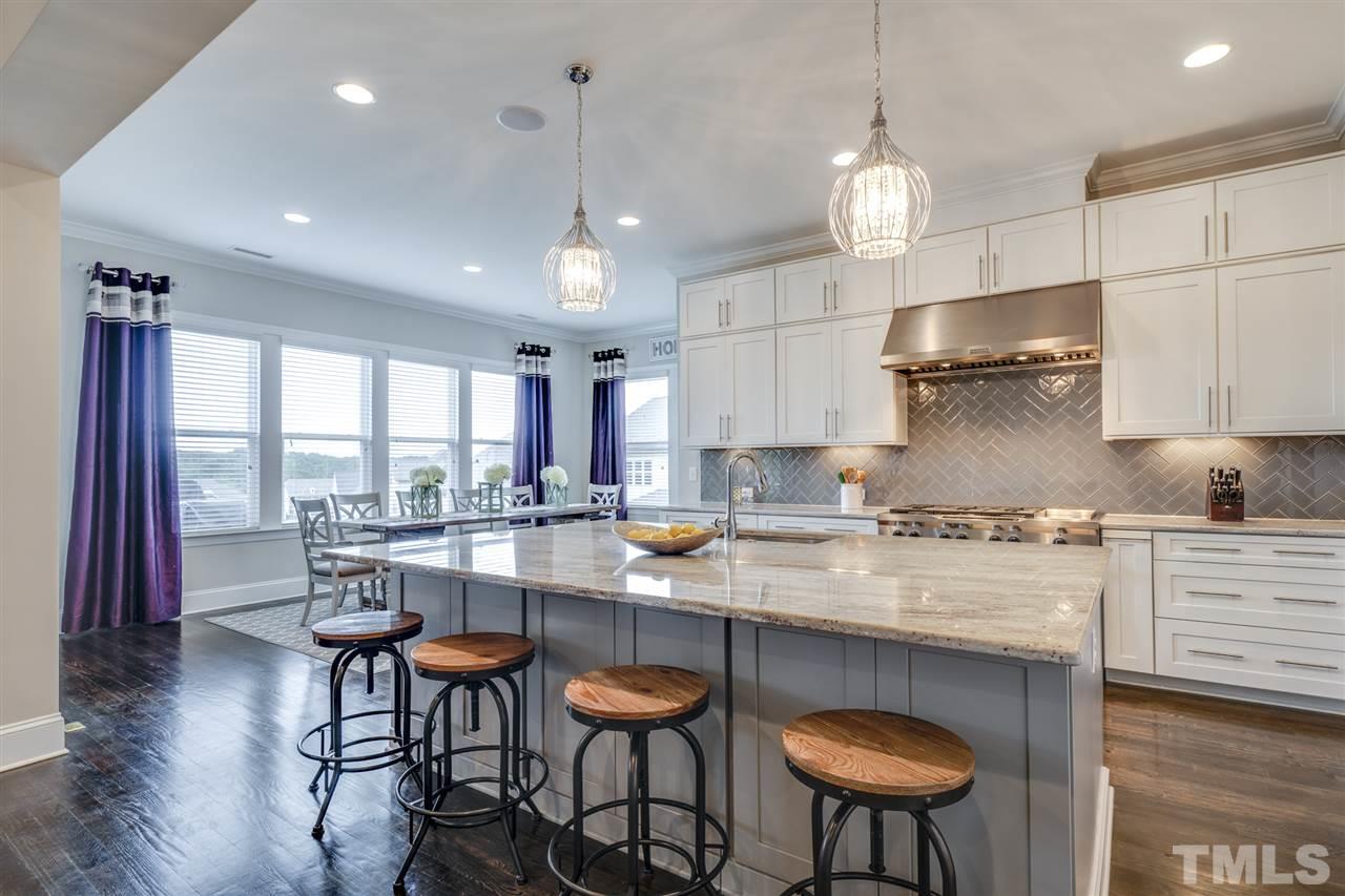 7504 Pinaster Place Raleigh, NC 27613 - Photo 5 of 30 a kitchen with stainless steel appliances granite countertop a stove a refrigerator a kitchen island a dining table and chairs with wooden floor