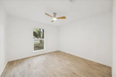 an empty room with wooden floor ceiling fan and windows