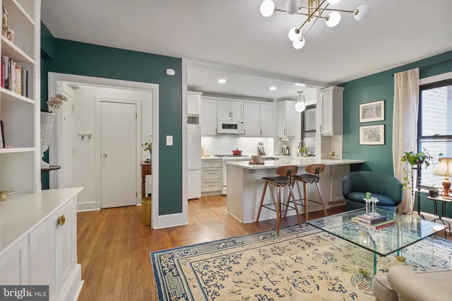 a living room with stainless steel appliances furniture a rug kitchen view and a table