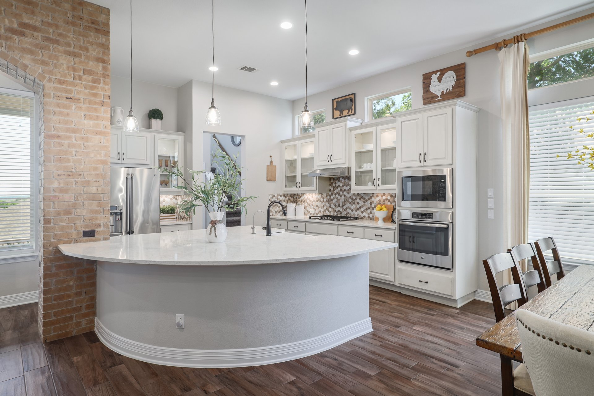 309 Rancho Sienna Loop Georgetown, TX 78628 - Photo 15 of 40 Kitchen featuring a large curved island with a white quartz countertop, stainless steel appliances, white cabinetry with glass-front uppers, a mosaic tile backsplash, and wood-finish flooring