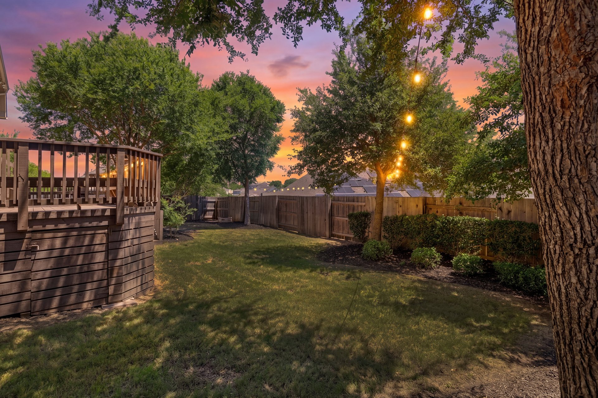 309 Rancho Sienna Loop Georgetown, TX 78628 - Photo 34 of 40 Expansive backyard featuring a manicured lawn, a multi-level wooden deck with railing, mature trees, string lighting, and perimeter fencing