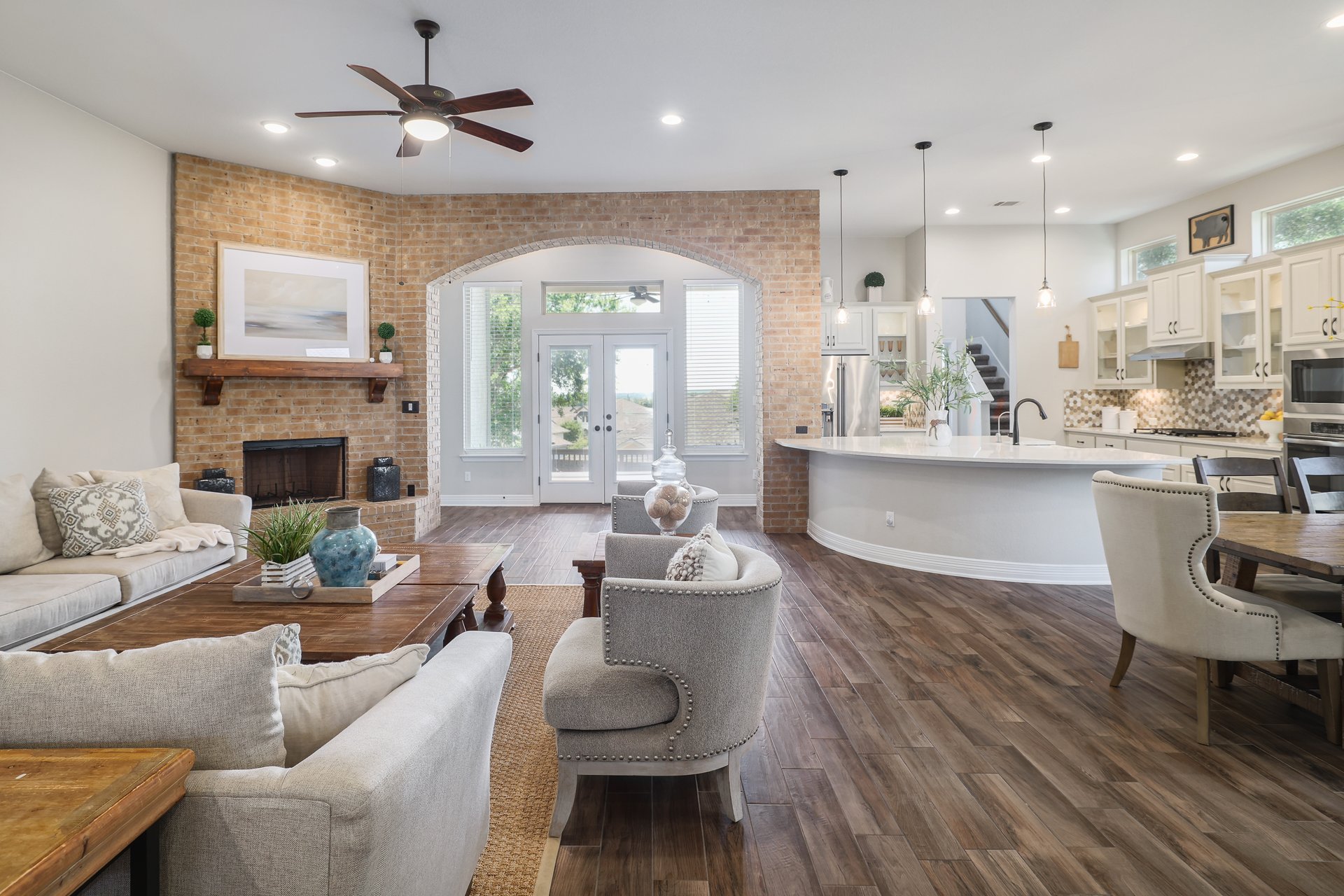 309 Rancho Sienna Loop Georgetown, TX 78628 - Photo 10 of 40 Spacious living area featuring wood-finish flooring, a brick fireplace with a wood mantle, and an arched doorway leading to outdoor access