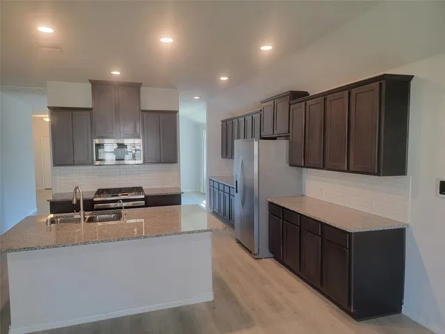 a kitchen with stainless steel appliances granite countertop a refrigerator a stove and a sink with wooden cabinets