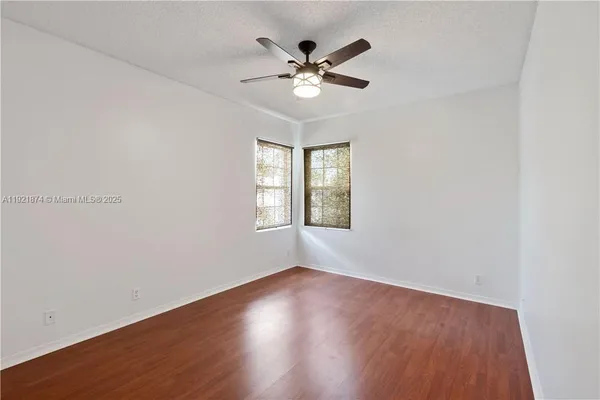 an empty room with wooden floor fan and windows