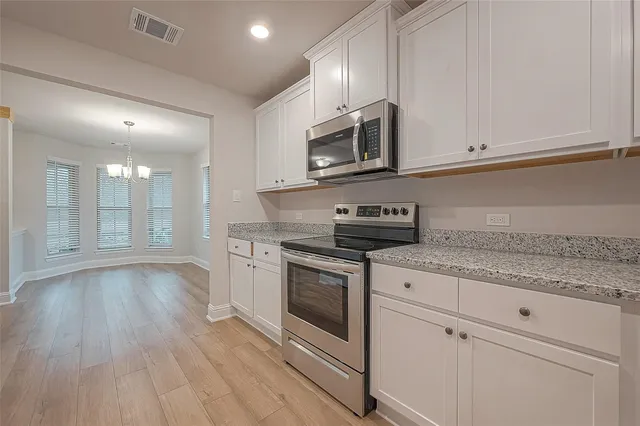 a kitchen with stainless steel appliances granite countertop a stove a microwave and white cabinets
