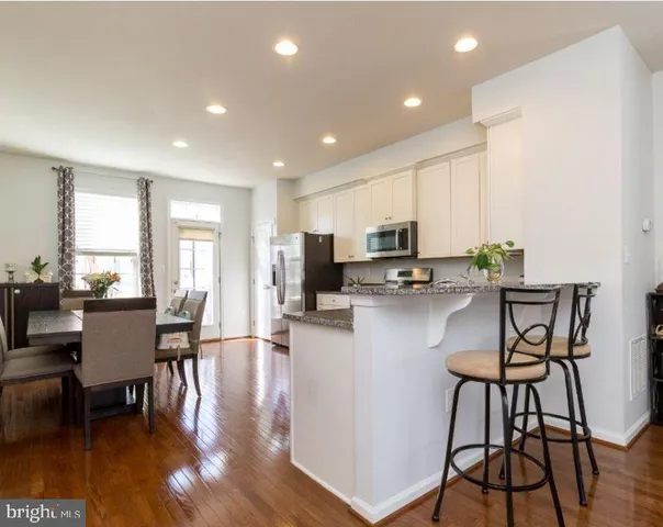 a kitchen with stainless steel appliances granite countertop a stove top oven a dining table and chairs with wooden floor