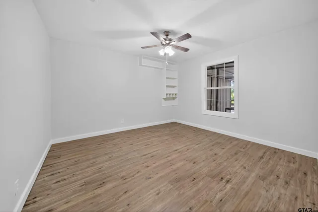 an empty room with wooden floor fan and windows