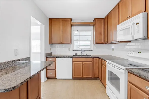 a kitchen with granite countertop white cabinets white stainless steel appliances a sink and a window