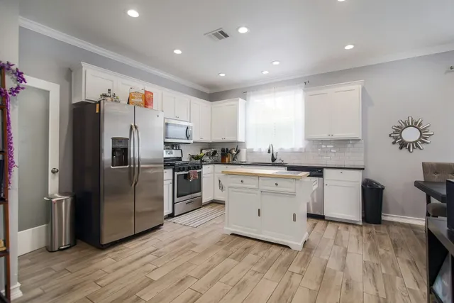 a kitchen with granite countertop a refrigerator oven a sink dishwasher and white cabinets with wooden floor