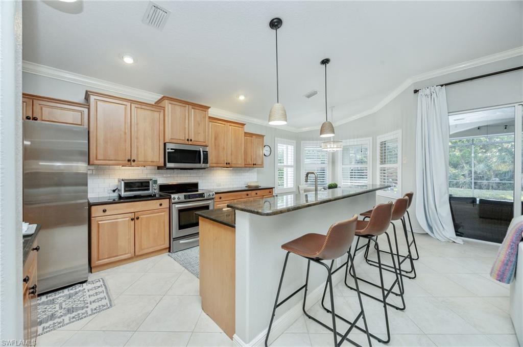 20350 Talon Trace Estero, FL 33928 - Photo 11 of 24 Kitchen featuring stainless steel appliances, ornamental molding, light tile patterned flooring, a kitchen bar, and dark stone counters
