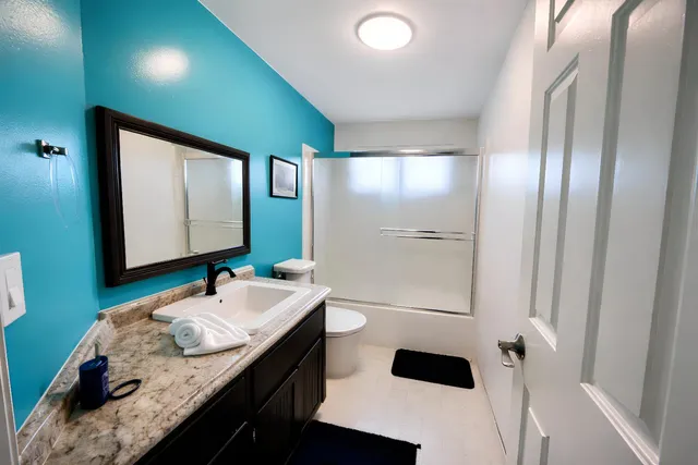 a bathroom with a granite countertop sink a toilet a mirror and shower