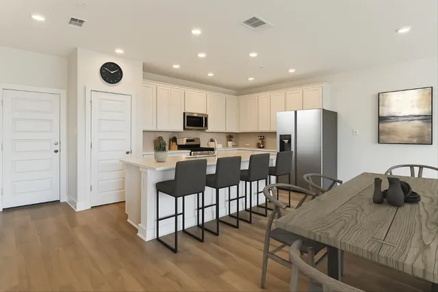 a kitchen with stainless steel appliances kitchen island granite countertop a refrigerator a stove a sink a oven with white cabinets and wooden floor