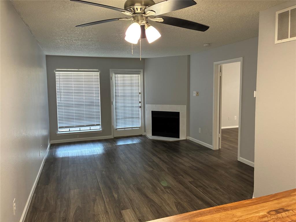 6108 Abrams Road, Unit 306 Dallas, TX 75231 - Photo 17 of 17 Unfurnished living room with a textured ceiling, a fireplace, ceiling fan, and dark wood finished floors