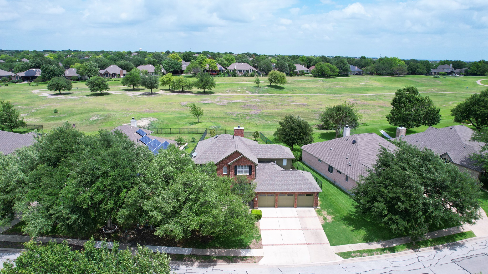 2408 Amen Corner Road Pflugerville, TX 78660 - Photo 2 of 40 Aerial perspective showcasing a brick residence with a multi-car garage, solar panels, and mature landscaping