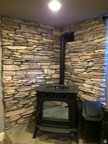 7030 West 2100 North Mendon, UT 84325 - Photo 64 of 67 Corner wood-burning stove with a decorative cast-iron facade, set against a stacked stone accent wall