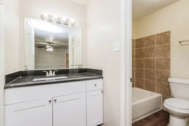 a bathroom with a granite countertop sink a toilet a mirror and bathtub