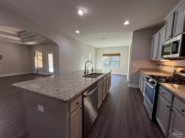 a kitchen with granite countertop kitchen island wooden floors wooden cabinets a sink and appliances