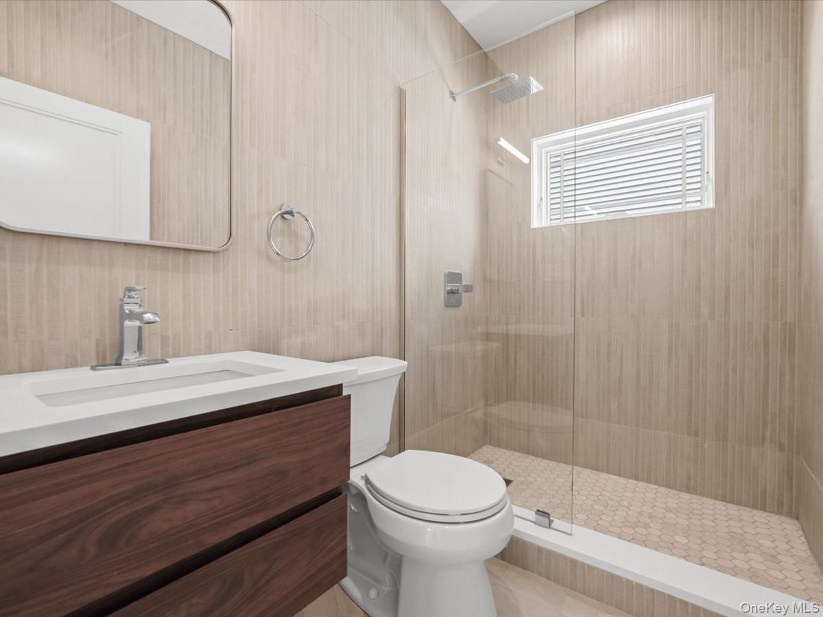 2849 Alder Road Bellmore, NY 11710 - Photo 13 of 34 Floating wood-finish vanity with an integrated rectangular sink, clear glass shower enclosure, rainfall showerhead, and light-toned vertical tile