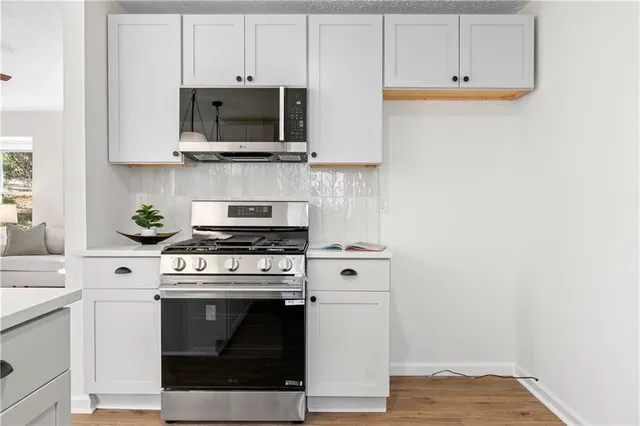 a kitchen with stainless steel appliances granite countertop a sink a window and white cabinets