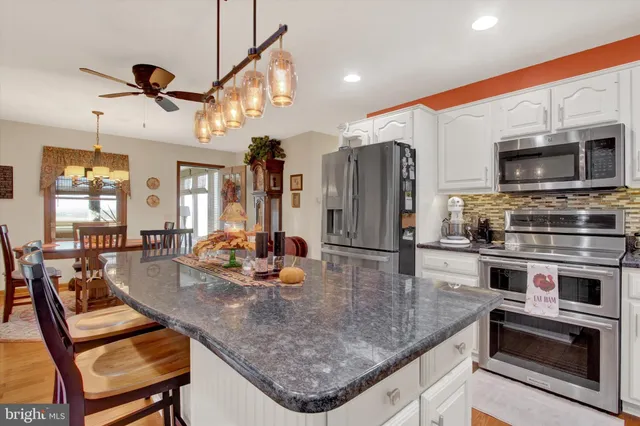 a kitchen with stainless steel appliances kitchen island granite countertop a refrigerator a stove top oven a sink dishwasher and white cabinets with wooden floor
