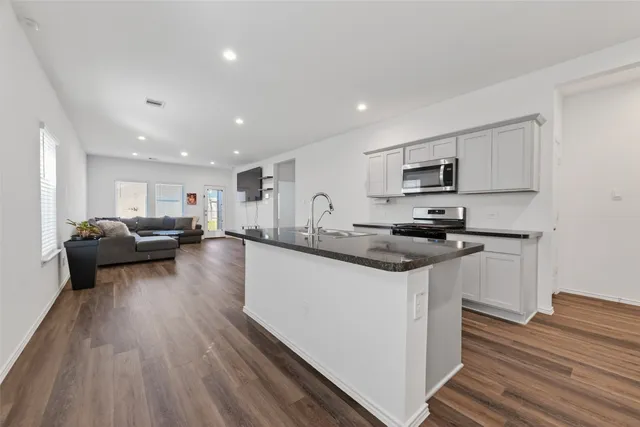 a living room with stainless steel appliances granite countertop wooden floors a stove and a sink