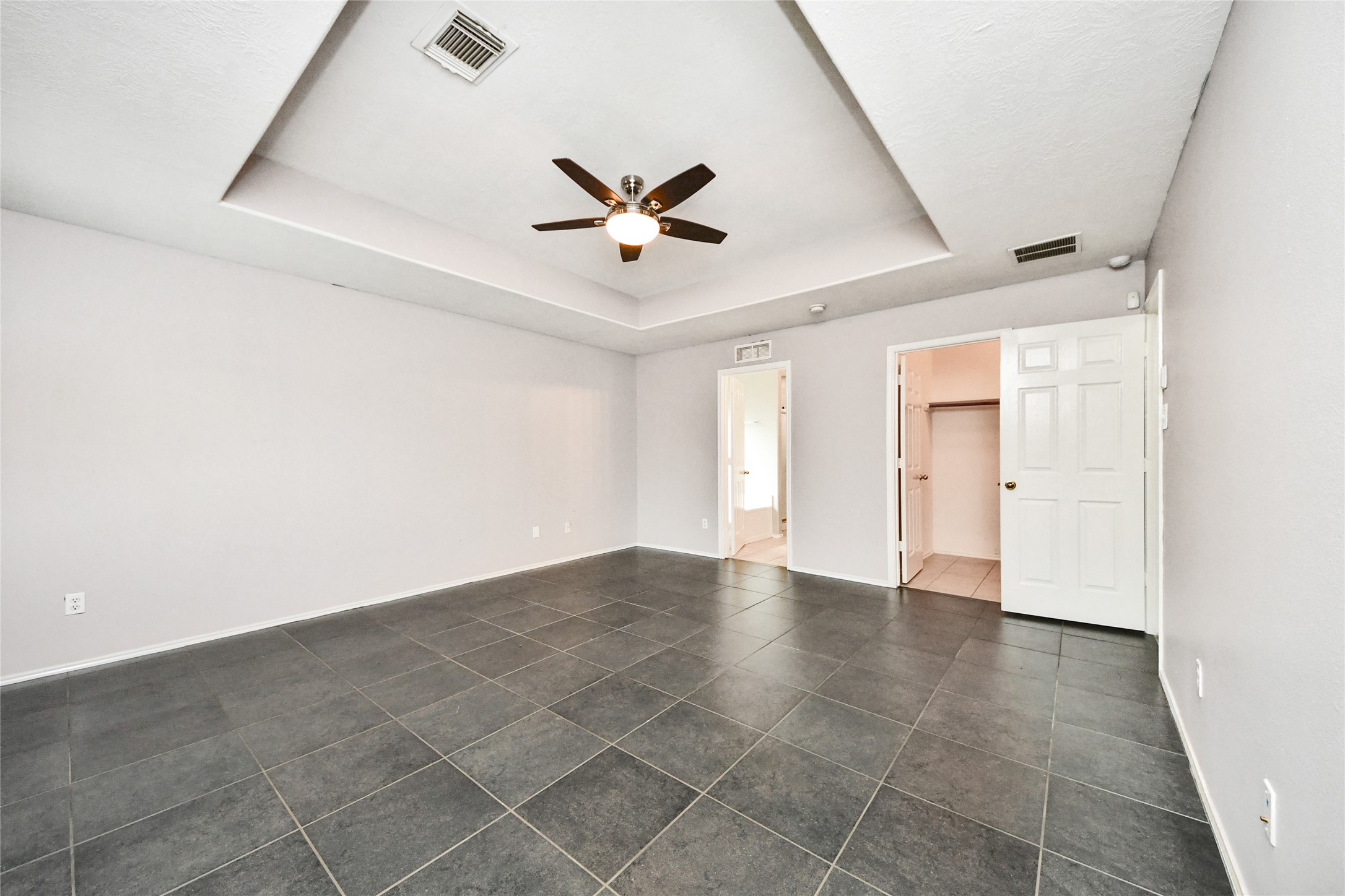 24019 Kingbriar Drive Spring, TX 77373 - Photo 28 of 41 This expansive primary suite features an elegant tray ceiling and large-format tile flooring, offering a clean and airy layout with direct access to the private ensuite bathroom.