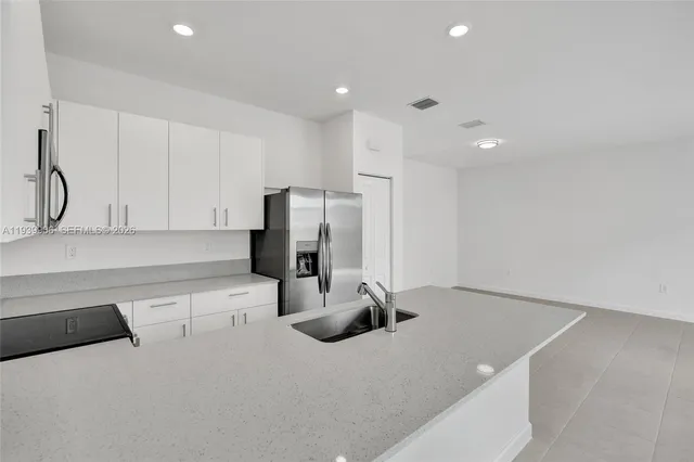 a kitchen with stainless steel appliances a sink a stove a microwave a refrigerator a sink and white cabinets