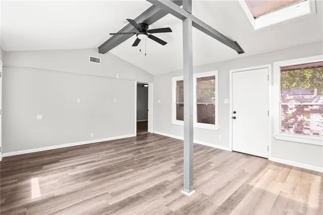 an empty room with wooden floor chandelier fan and windows