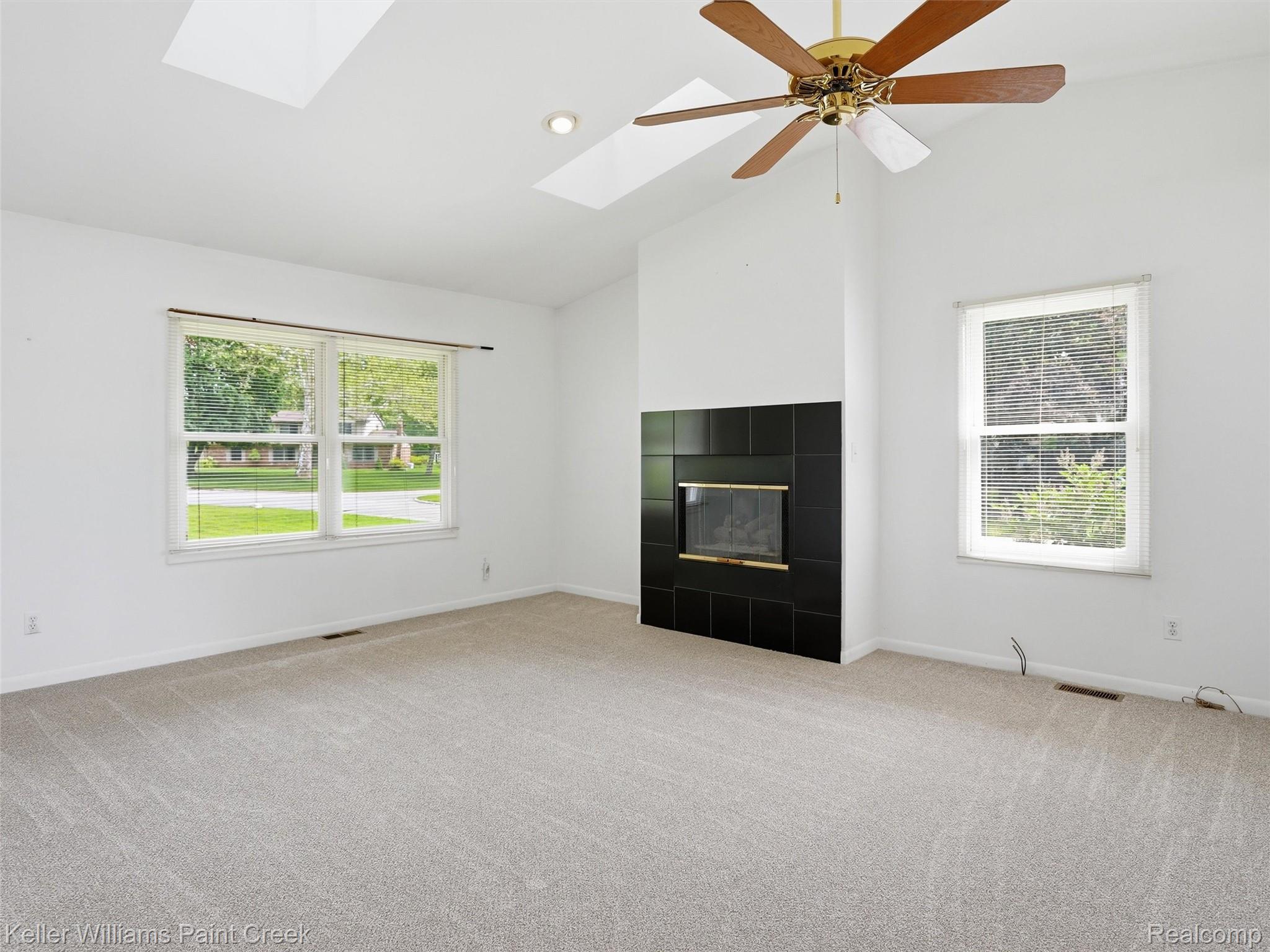 436 Broadleaf Drive Rochester, MI 48306 - Photo 21 of 41 Unfurnished living room with light carpet, a skylight, ceiling fan, a tiled fireplace, and vaulted ceiling
